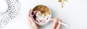 Person-Mixing-Cereal,-Milk,-and-Strawberry-Jam-on-White-Ceramic-Bowl